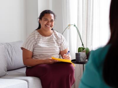 A woman sits and smiles while holding a pad and pen